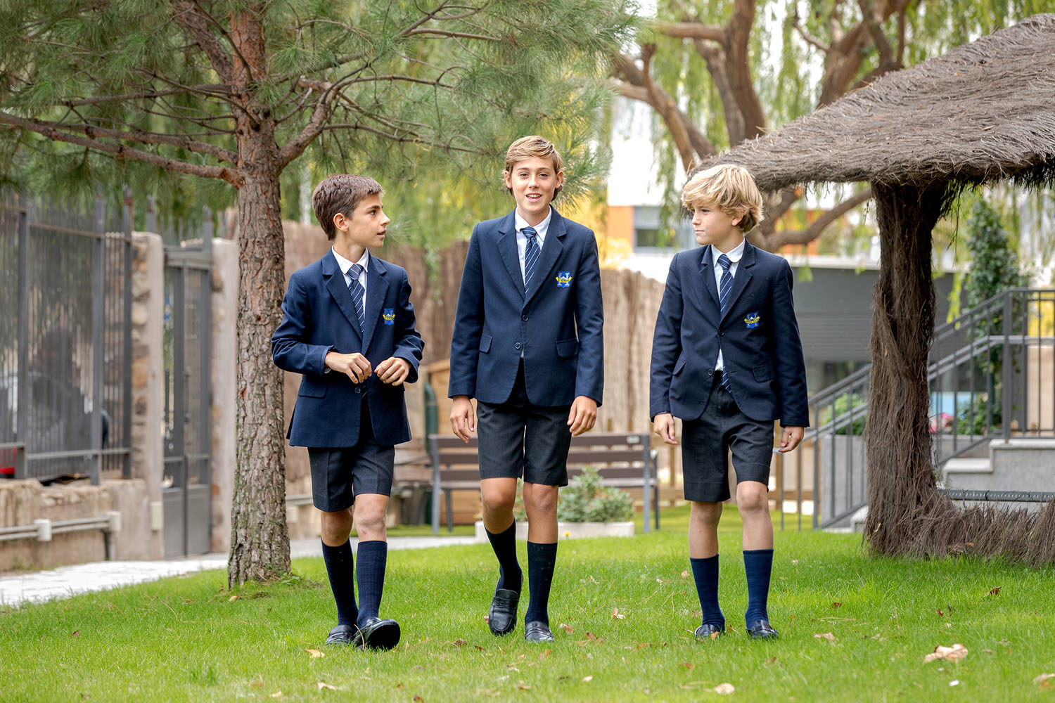 Tres alumnos en uniforme caminando por el jardín del colegio